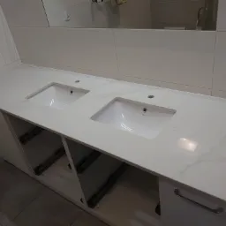 Biały blat z dwoma umywalkami w łazience, widoczne szuflady z systemem cichego domykania i odbicie w lustrze.