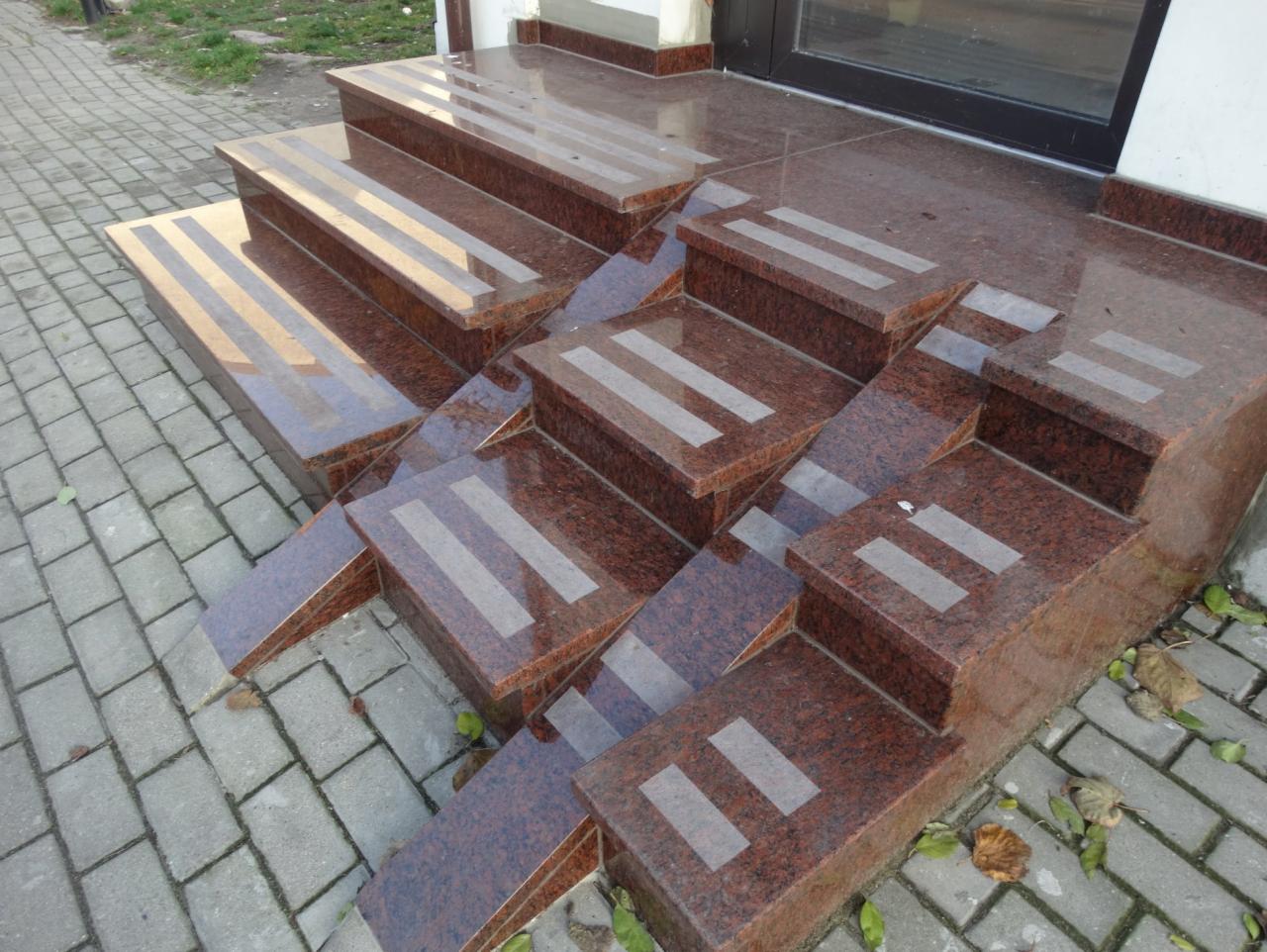 Zewnętrzne schody z czerwonego granitu z antypoślizgowymi paskami, prowadzące do drzwi wejściowych.