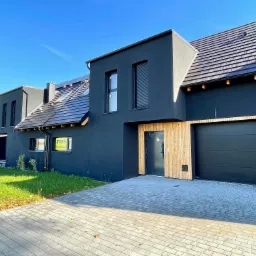 Szeregówka nowoczesnych, czarnych domów z drewnianymi akcentami elewacji i kostką brukową na podjeździe, w słoneczny dzień.