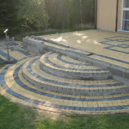 Układanie kostki brukowej w ogrodzie: schody i ścieżka w kolorach żółtym i szarym. Częściowo ukończona praca, widoczne niedokończone fragmenty ścieżki.