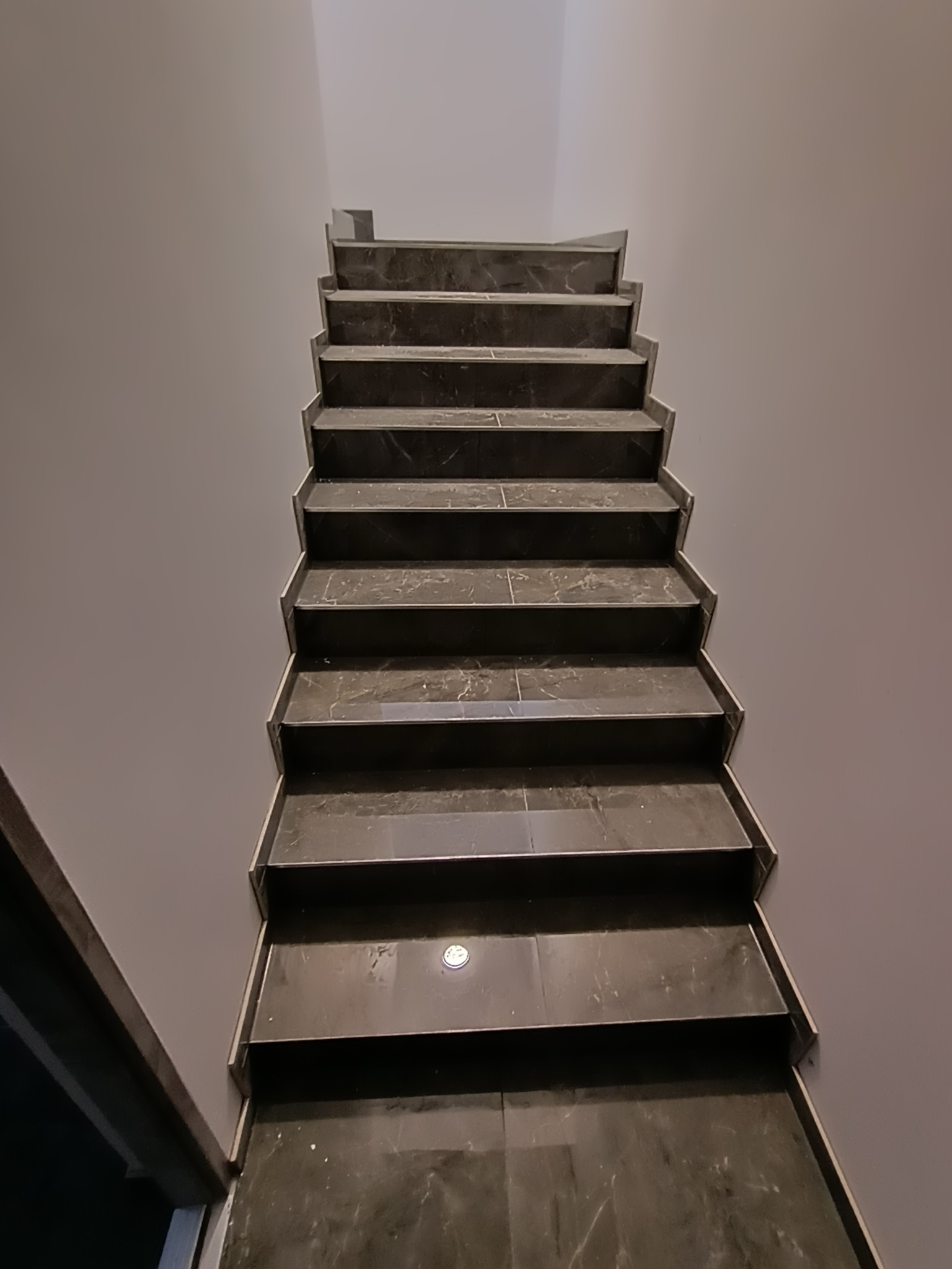 Schody wykończone ciemnym marmurem, widok z dołu, oświetlenie punktowe na dolnym stopniu.
