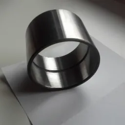 Metalowy pierścień tulejowy z widocznymi śladami obróbki na wewnętrznej powierzchni, leżący na białej kartce papieru w neutralnym oświetleniu.