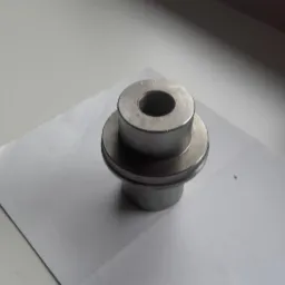 Metalowy element z otworem na białym tle, widoczne ślady obróbki.