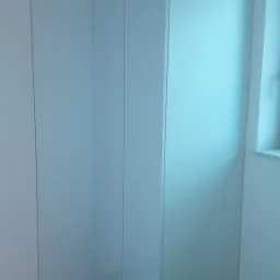 Biała szafa wnękowa z połyskującymi frontami, widoczna z perspektywy podłogi, z fragmentem okna po prawej stronie.