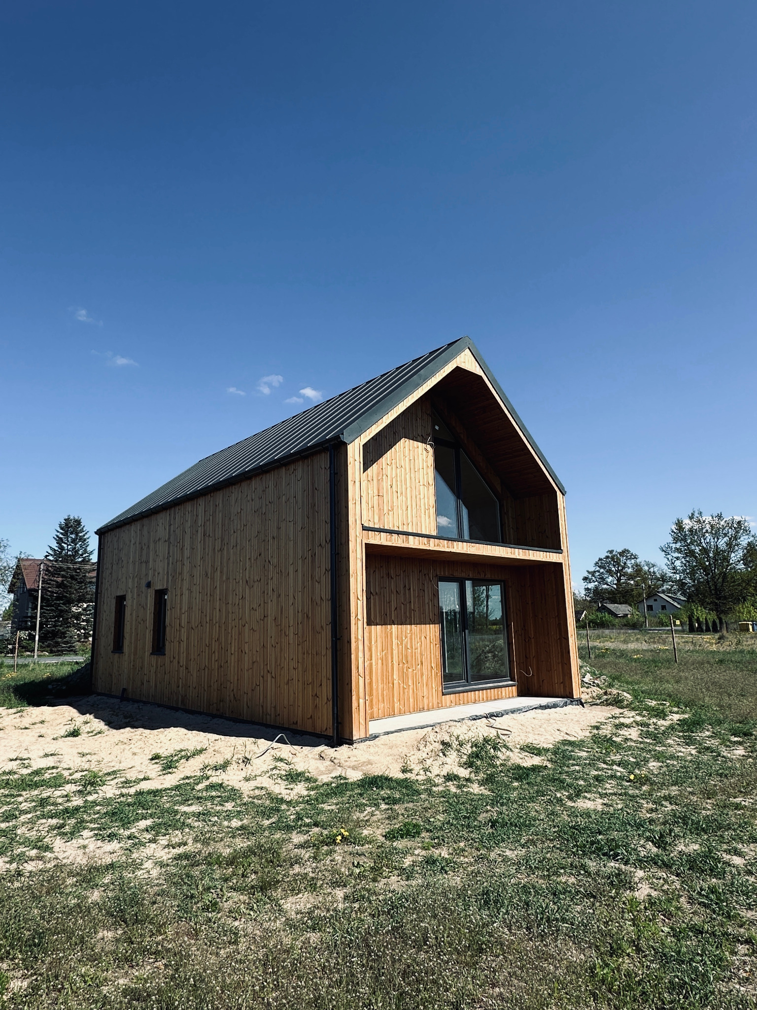 Nowoczesny dom z drewnianą elewacją i dużymi oknami, otoczony zielenią i piaskiem. Widok z dołu podkreśla geometrię budynku.