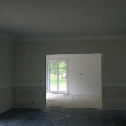 KAMIL WILCZYŃSKI ARCHITEKTURA I BUDOWNICTWO - Pokój w trakcie malowania, zabezpieczony folią, z widocznymi listwami dekoracyjnymi i przygotowanymi ścianami.