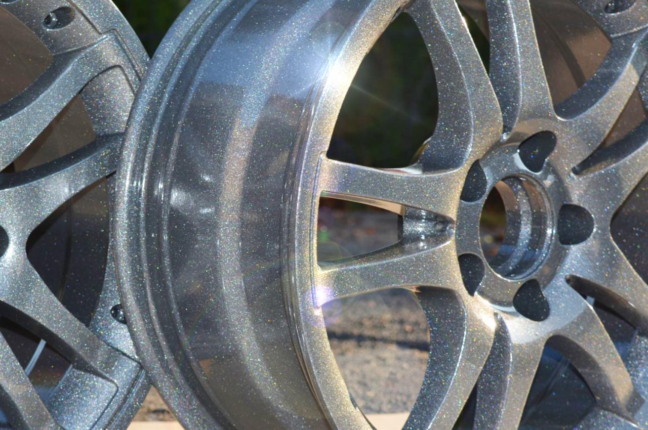 Dwa aluminiowe felgi samochodowe z efektem metalicznego połysku, prawdopodobnie po obróbce strumieniowo-ściernej i nałożeniu farby, z widocznym detalem szprych i mocowań.