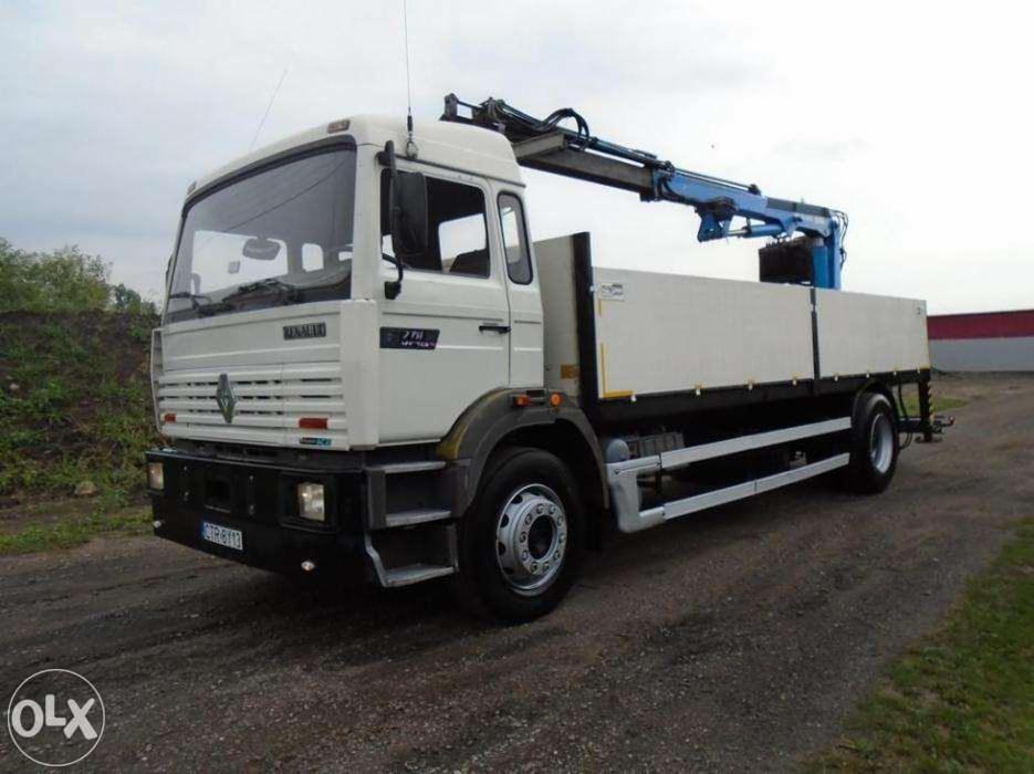 Biała ciężarówka Renault 770 z niebieskim dźwigiem HDS na platformie. Pojazd stoi na żwirowej nawierzchni, w tle zieleń i budynek. Dzień, pochmurno.