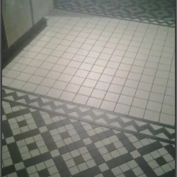 Ukończona podłoga z jasnych kwadratowych płytek, obramowana wzorem z ciemnych i jasnych kwadratów, oddzielonych zygzakowatym pasem. Widok z góry.