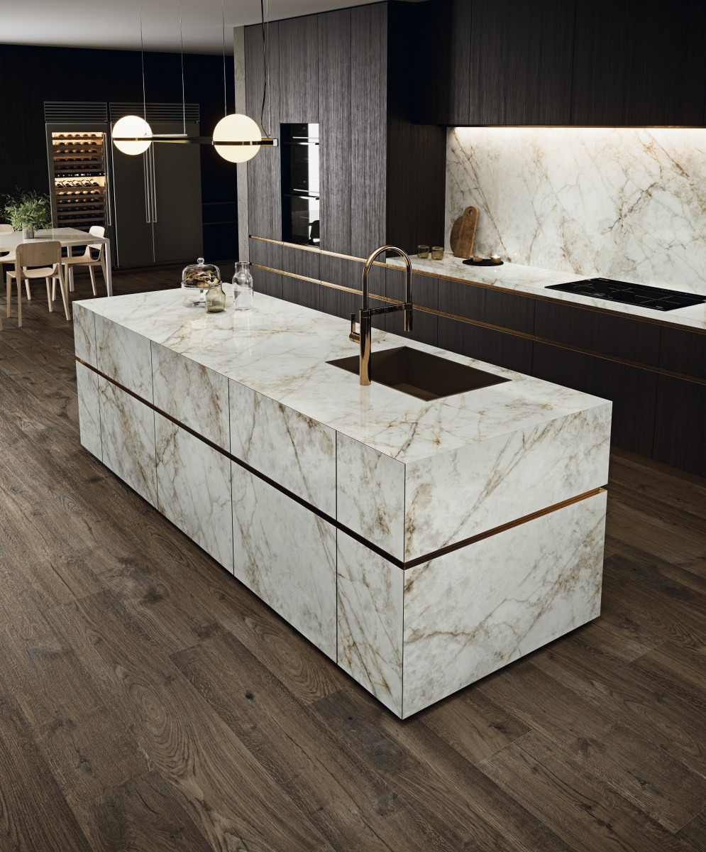 Nowoczesna kuchnia z wyspą pokrytą marmurkowym blatem, złota bateria i ciemne drewniane szafki w tle, oświetlenie punktowe, podłoga z ciemnego drewna.