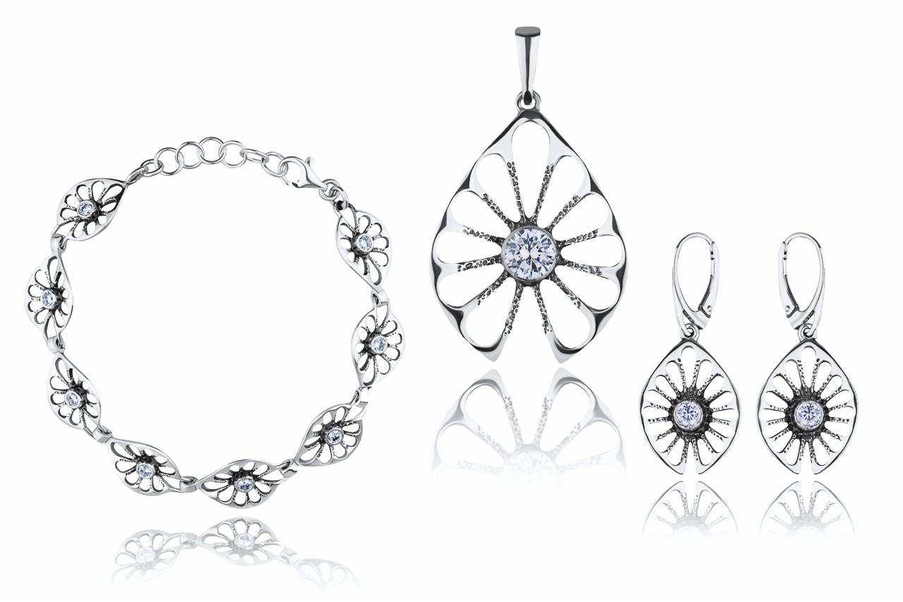 Srebrny komplet biżuterii z kwiatowym motywem, składający się z bransoletki, wisiorka i kolczyków, na białym tle z odbiciem.