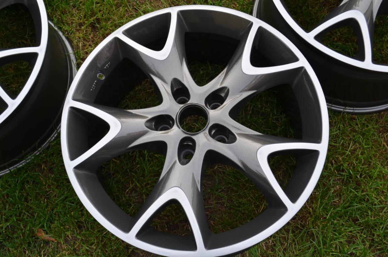 Pomalowana felga aluminiowa w odcieniach szarości i bieli, z widoczną fakturą lakieru, leżąca na trawie.