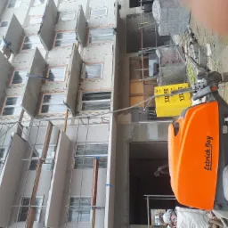 Pomarańczowa maszyna do wylewek marki Estrich Boy na placu budowy wielopiętrowego budynku w trakcie prac wykończeniowych.