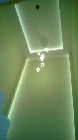 Nowoczesny sufit podwieszany z oświetleniem LED i designerską lampą wiszącą w odcieniach zieleni. Minimalistyczny design.