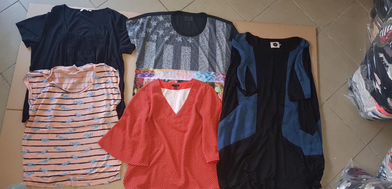 Stos ubrań damskich, w tym bluzka w różowe paski z motywem niebieskich ptaków, czerwona bluzka w białe kropki z szerokimi rękawami, czarna bluzka z koronkową wstawką i tunika w czarno-niebieskie...