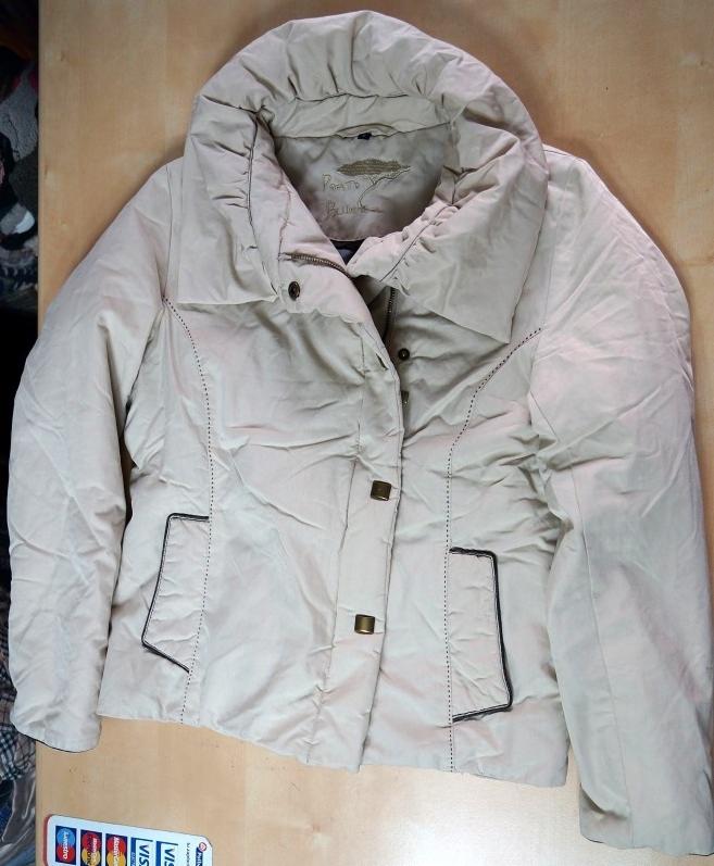 Beżowa, pikowana kurtka zimowa z dużym kołnierzem, zapinana na kwadratowe guziki. Widoczne imitacje kieszeni z ciemną lamówką i przeszycia wzdłuż rękawów.