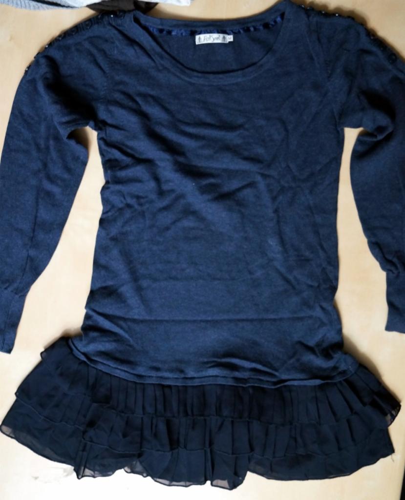 Granatowa tunika z długim rękawem i falbaną na dole, ozdobiona drobnymi koralikami na ramionach, leży na płaskiej powierzchni.