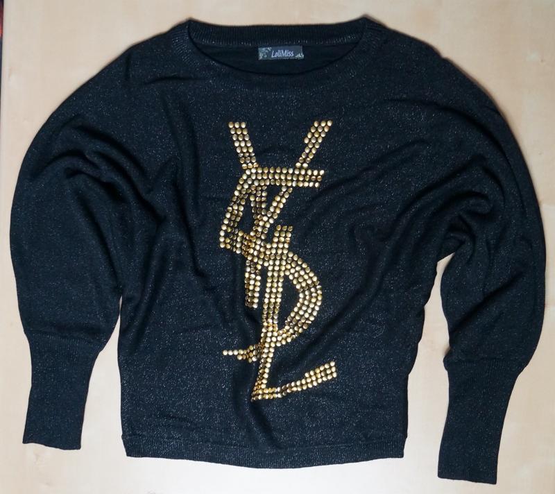 Czarny sweter z długimi rękawami, zdobiony złotym logo YSL z ćwieków, na jednolitym tle. Widoczne logo marki LaliMiss w lewym górnym rogu.