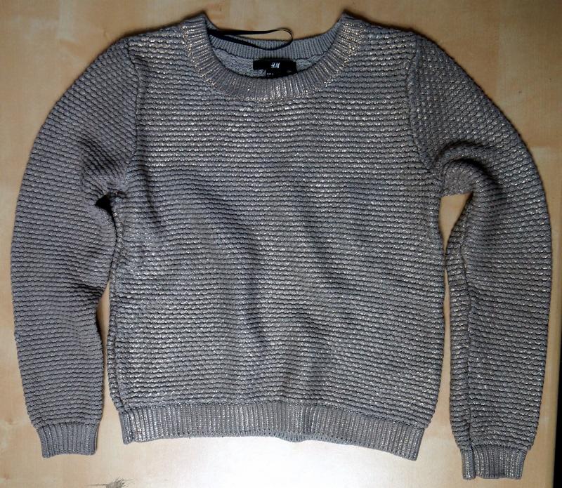 Szary sweter H&M z delikatną, złotą nitką i wyraźną fakturą leży na jasnym podłożu, prezentując swój unikalny wzór i markę.