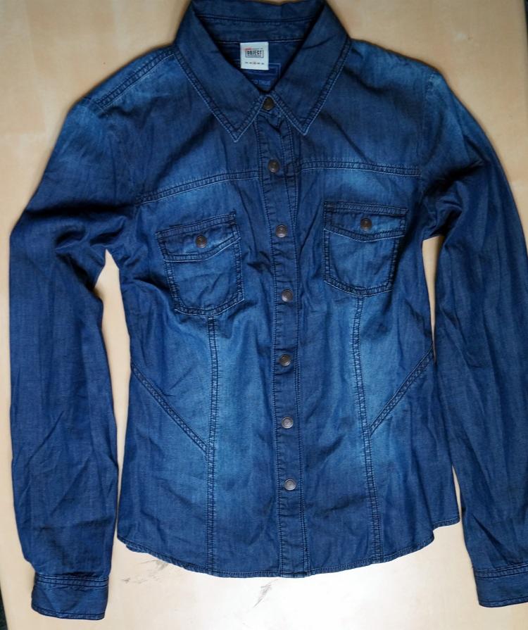 Damska koszula jeansowa z długim rękawem, zapinana na guziki, z dwiema kieszeniami na piersiach, w odcieniu ciemnego denimu, leżąca na płaskiej powierzchni.