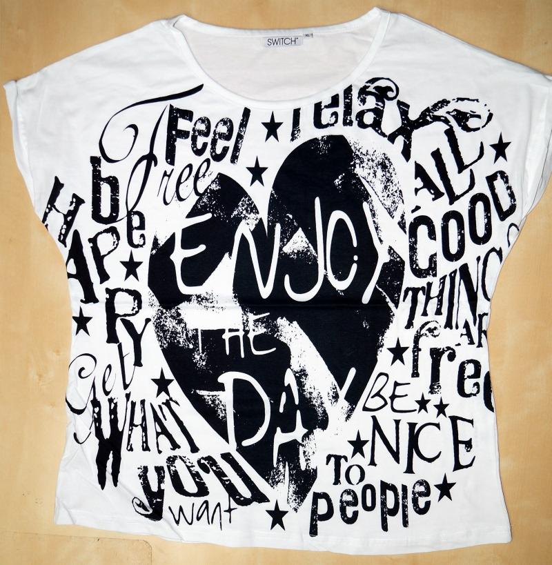 Biała koszulka z krótkim rękawem, ozdobiona czarnymi napisami i grafikami, leży na płaskiej powierzchni. Widoczny napis 'SWITCH' na karku.