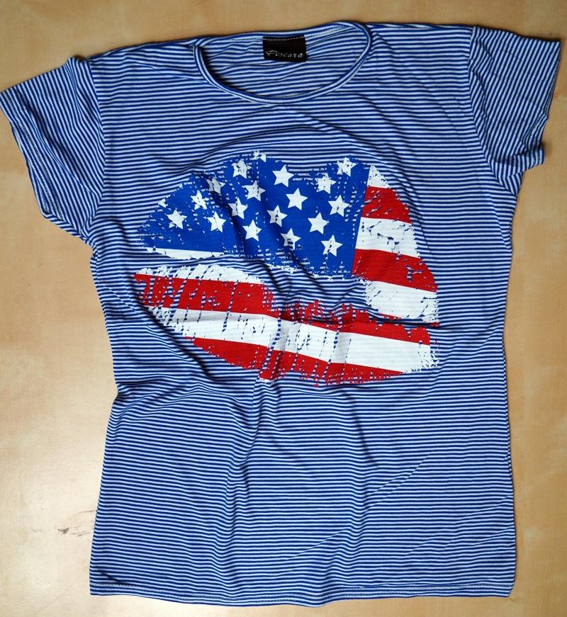 Pasiasta koszulka w odcieniach błękitu z nadrukiem ust w barwach flagi USA. Używana odzież z unikalnym wzorem, leżąca na płaskiej powierzchni.