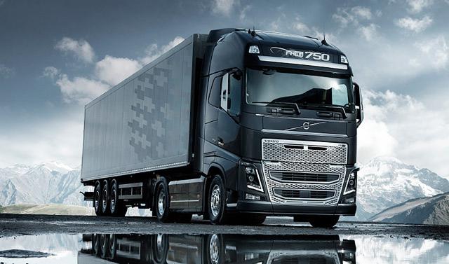 Czarna ciężarówka Volvo FH16 750 z naczepą na tle gór. Na asfalcie widoczne kałuże z odbiciem pojazdu. Naczepa z delikatnym wzorem.