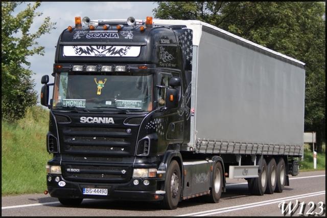 Czarna ciężarówka Scania R500 z naczepą na drodze, widok z przodu, ozdobiona grafikami, tablica rejestracyjna z Polski.