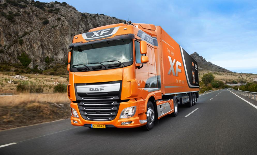Pomarańczowa ciężarówka DAF XF na drodze, góry w tle. Widoczny numer rejestracyjny. Perspektywa z dołu, podkreślająca wielkość pojazdu.