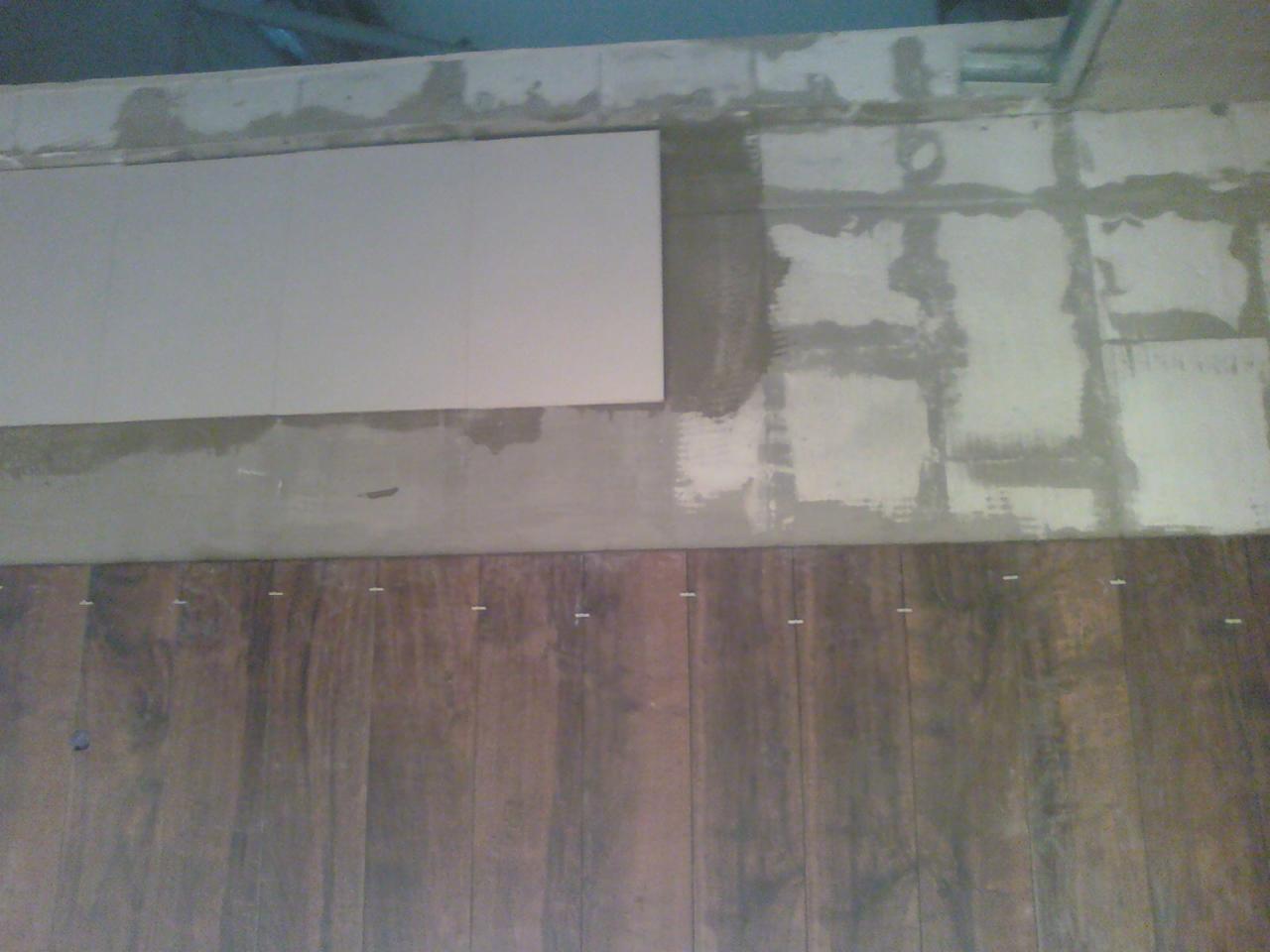 Układanie paneli podłogowych w trakcie: widoczne deski z dystansami, fragment płyty i ślady kleju na podłożu. Ujęcie z góry, bliski kadr.