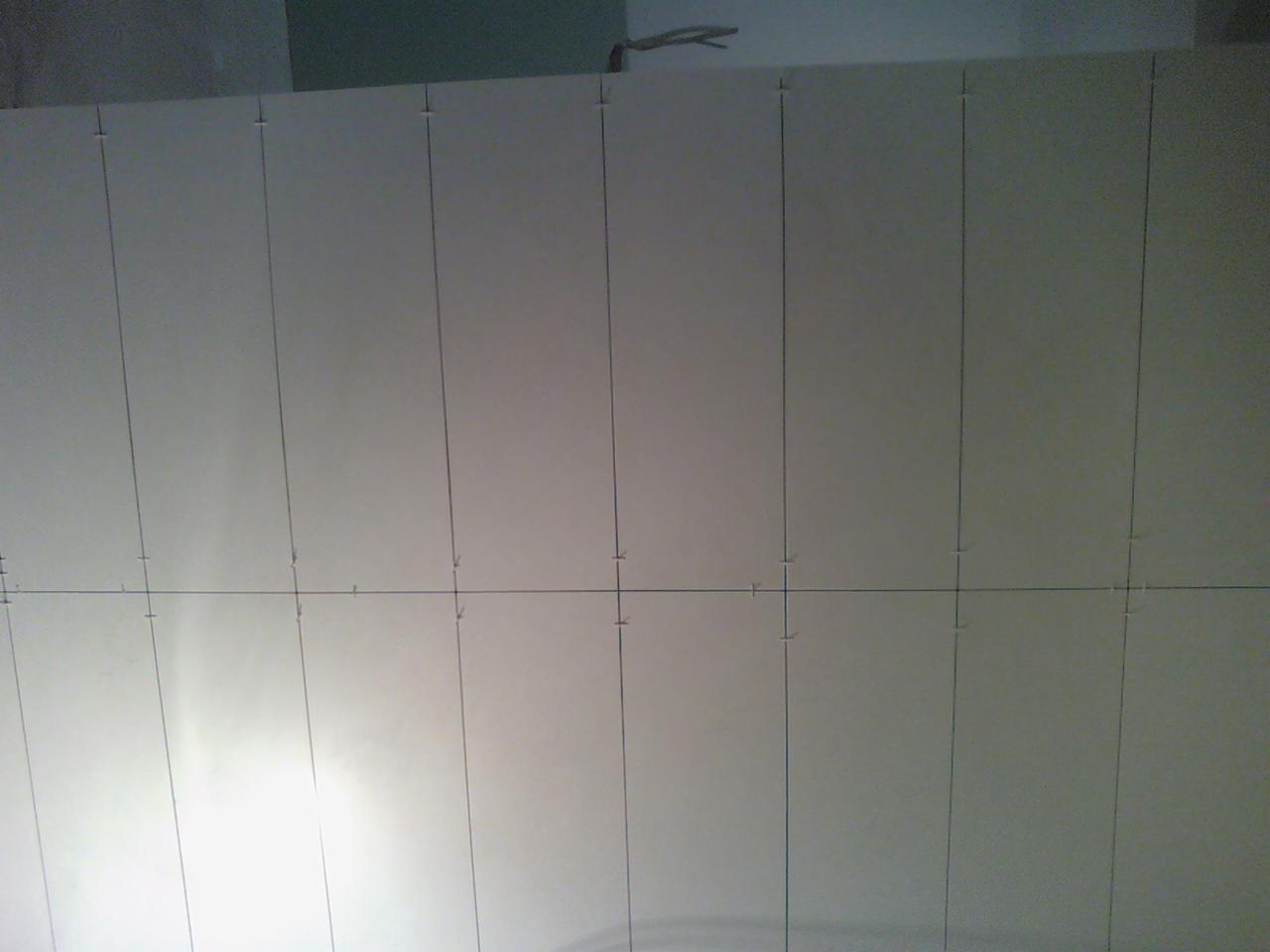 Ściana z przyklejonymi płytami izolacyjnymi, widoczne pionowe i poziome linie wyznaczające podział, przygotowane do dalszych prac wykończeniowych.