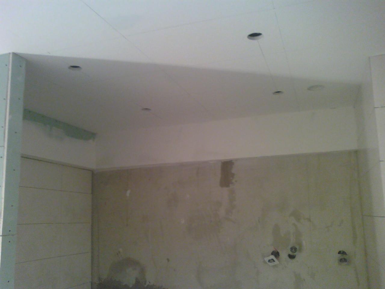 Wnętrze w trakcie wykańczania: sufit podwieszany z otworami na oświetlenie, ściany przygotowane do malowania, widoczne puszki elektryczne.