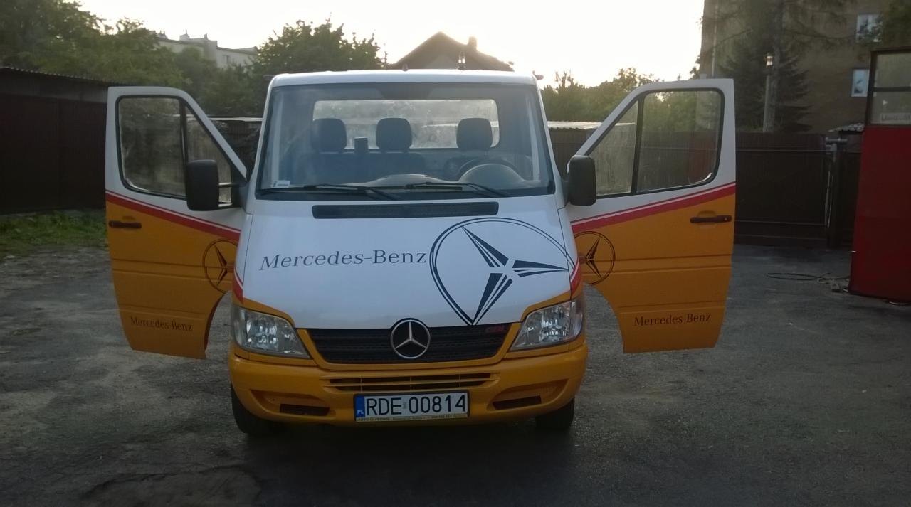 Żółto-biały bus Mercedes-Benz z otwartymi drzwiami, widok z przodu, tablica rejestracyjna RDE 00814. Widoczne logo Mercedes-Benz na masce i drzwiach.