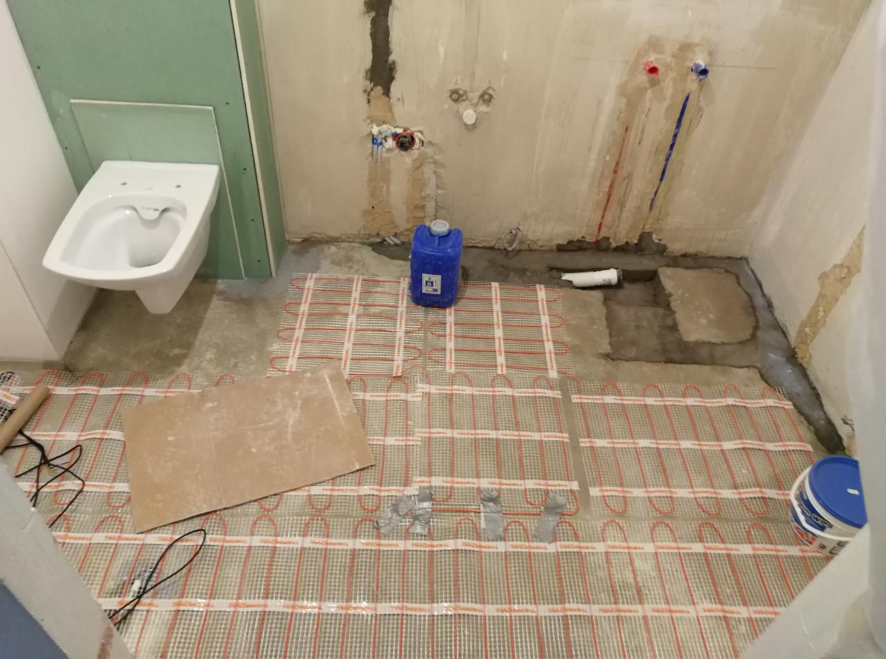 Montaż ogrzewania podłogowego w łazience w trakcie remontu, widoczne maty grzewcze, nieotynkowane ściany z wyprowadzonymi instalacjami, podwieszana toaleta na stelażu.