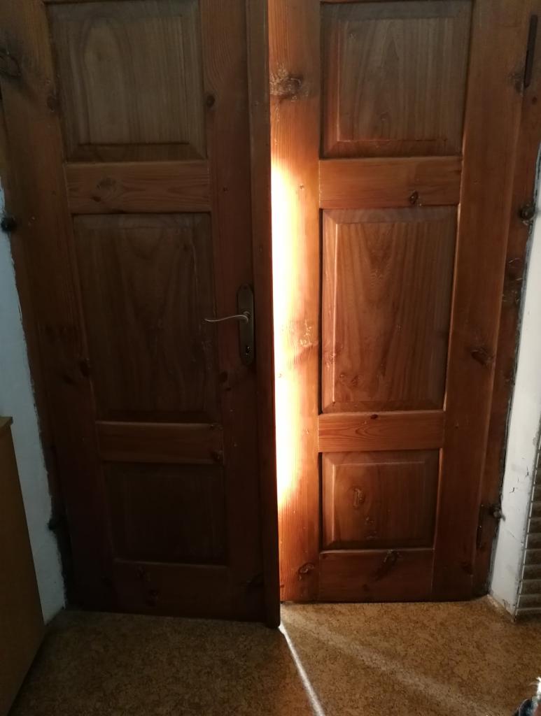 Dwuskrzydłowe, drewniane drzwi wewnętrzne z widocznym prześwitem światła między skrzydłami, ukazujące fragment podłogi.