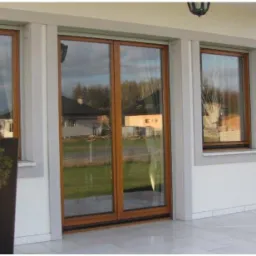 Eleganckie okna z drewnianymi ramami i szarymi parapetami w nowoczesnym domu. Widok na ogród odbija się w szybach.