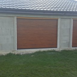 PHTU CONTROL - Dwie brązowe bramy garażowe segmentowe oraz drzwi wejściowe o identycznym wzorze, zamontowane w surowym, betonowym budynku z szarą dachówką.