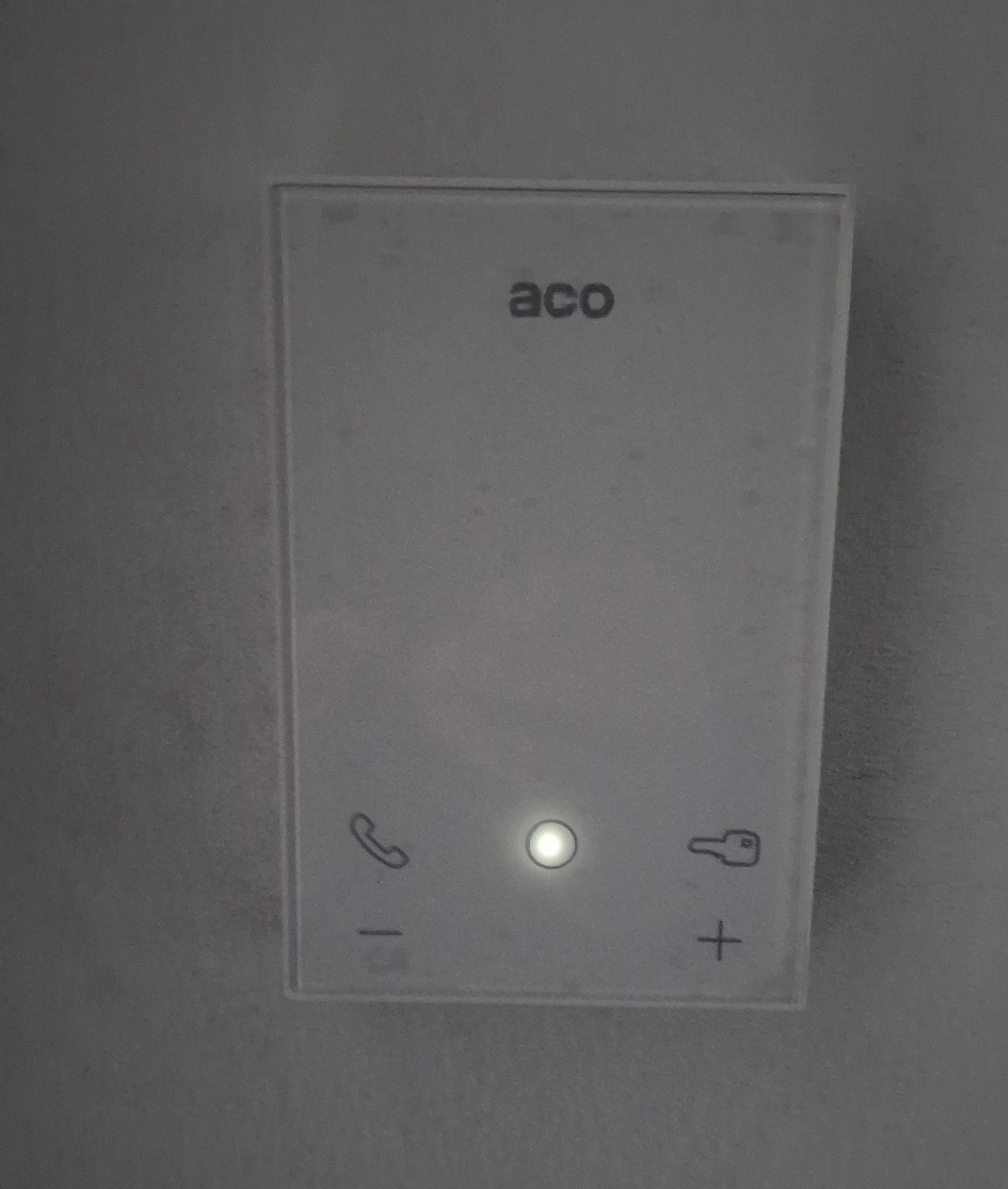 Panel domofonu ACO z podświetlonym przyciskiem, widoczne ikony telefonu i klucza.
