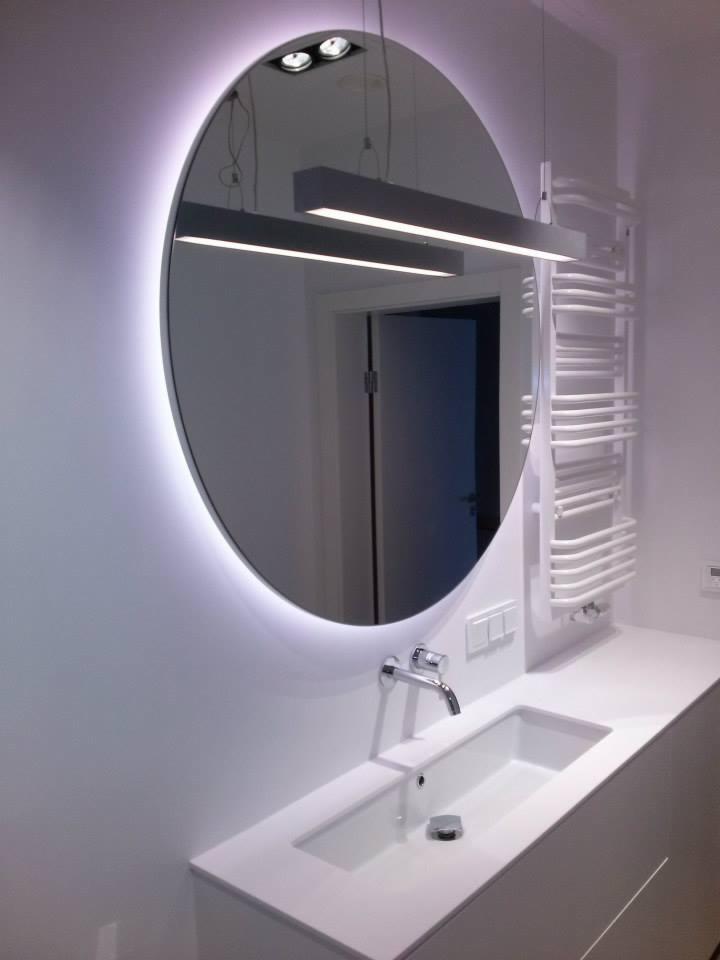 Nowoczesna łazienka z owalnym lustrem podświetlanym LED, białą umywalką wpuszczaną w blat i grzejnikiem drabinkowym w tle.