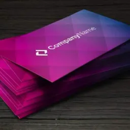 Stos wizytówek z gradientem kolorów od niebieskiego do różowego, leżący na ciemnym, drewnianym tle.