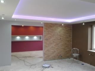 Pokój po malowaniu ścian z oświetleniem LED na suficie, widoczne ślady po remoncie na podłodze, ściana akcentowa w kolorze czerwonym z wnęką i oświetleniem punktowym, obok ściana wykończona...