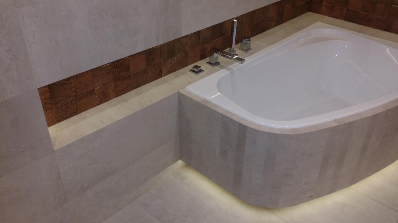 Nowoczesna, biała wanna z chromowaną armaturą, obudowana płytkami w odcieniach beżu i brązu z podświetleniem LED u dołu w łazience.