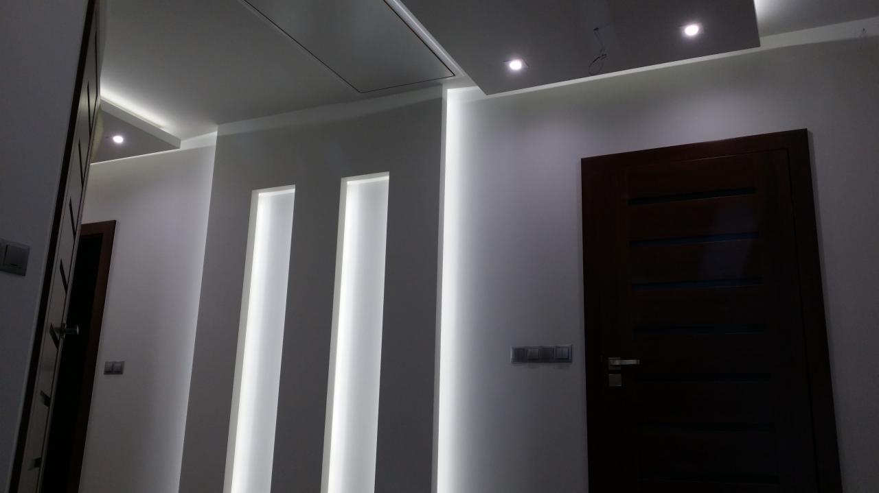 Nowoczesne wnętrze z podświetlanymi wnękami ściennymi i ciemnymi drzwiami, oświetlenie sufitowe punktowe.