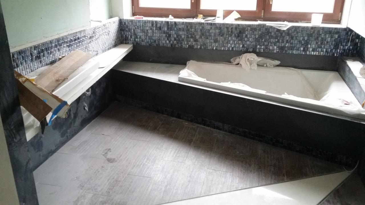 Łazienka w trakcie prac wykończeniowych: ułożona mozaika na ścianie, częściowo położona podłoga z płytek imitujących drewno, wanna zabezpieczona folią, widoczne kartony i narzędzia.