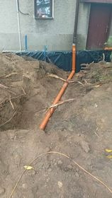 Brązowa rura spustowa w wykopie ziemnym, prawdopodobnie przygotowanie do odprowadzenia wody od fundamentów budynku.