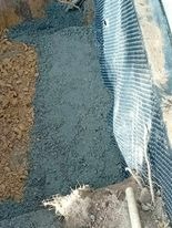 Wyłożony geowłókniną wykop pod fundament, zasypany warstwą drenażową z grysu. Widoczne krawędzie wykopu i fragment rury drenażowej.