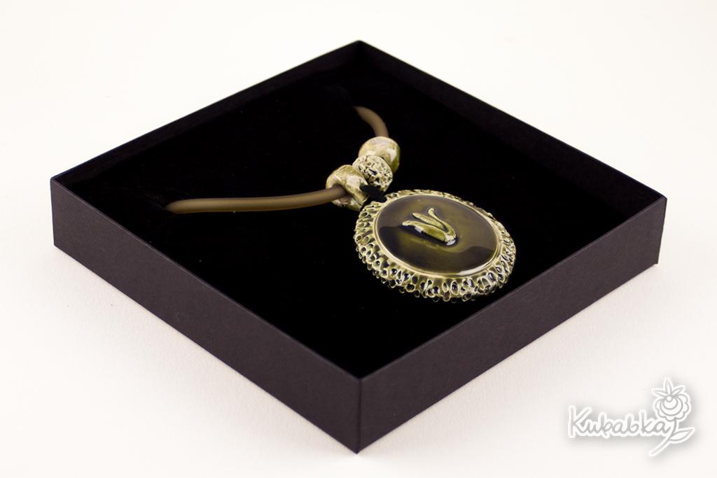 Ozdobny, okrągły wisiorek z symbolem w pudełku prezentowym, wykonany w odcieniach zieleni i złota, prezentowany na czarnym aksamitnym tle w eleganckim pudełku.