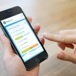 Osoba korzysta z aplikacji mobilnej Flygappen do wyszukiwania lotów na smartfonie, wprowadzając dane lotu z Warszawy Modlin do Oslo Rygge. Widoczny ekran z polami wyboru daty i liczby pasażerów.