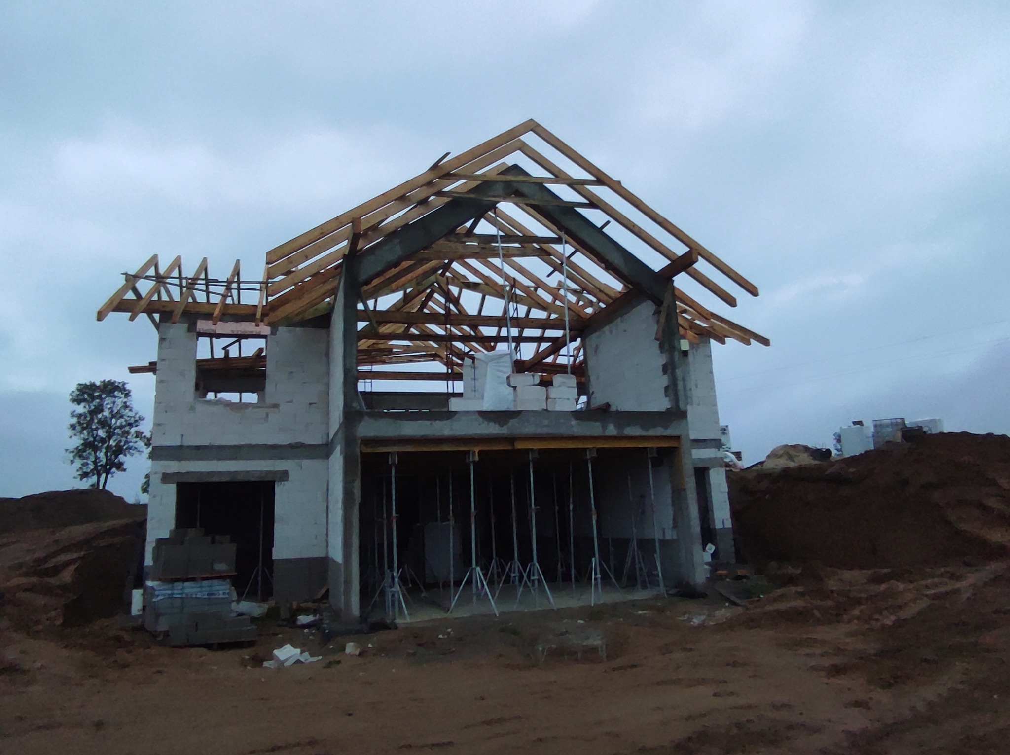 Stan surowy otwarty domu jednorodzinnego w Czarne, widoczne drewniane elementy konstrukcji dachu, ściany z bloczków, podpory szalunkowe oraz sterta ziemi w tle.