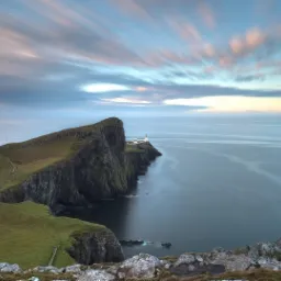 Panoramiczny widok na klif z latarnią morską w oddali, miękkie światło zachodzącego słońca rozmywa chmury nad spokojnym oceanem.